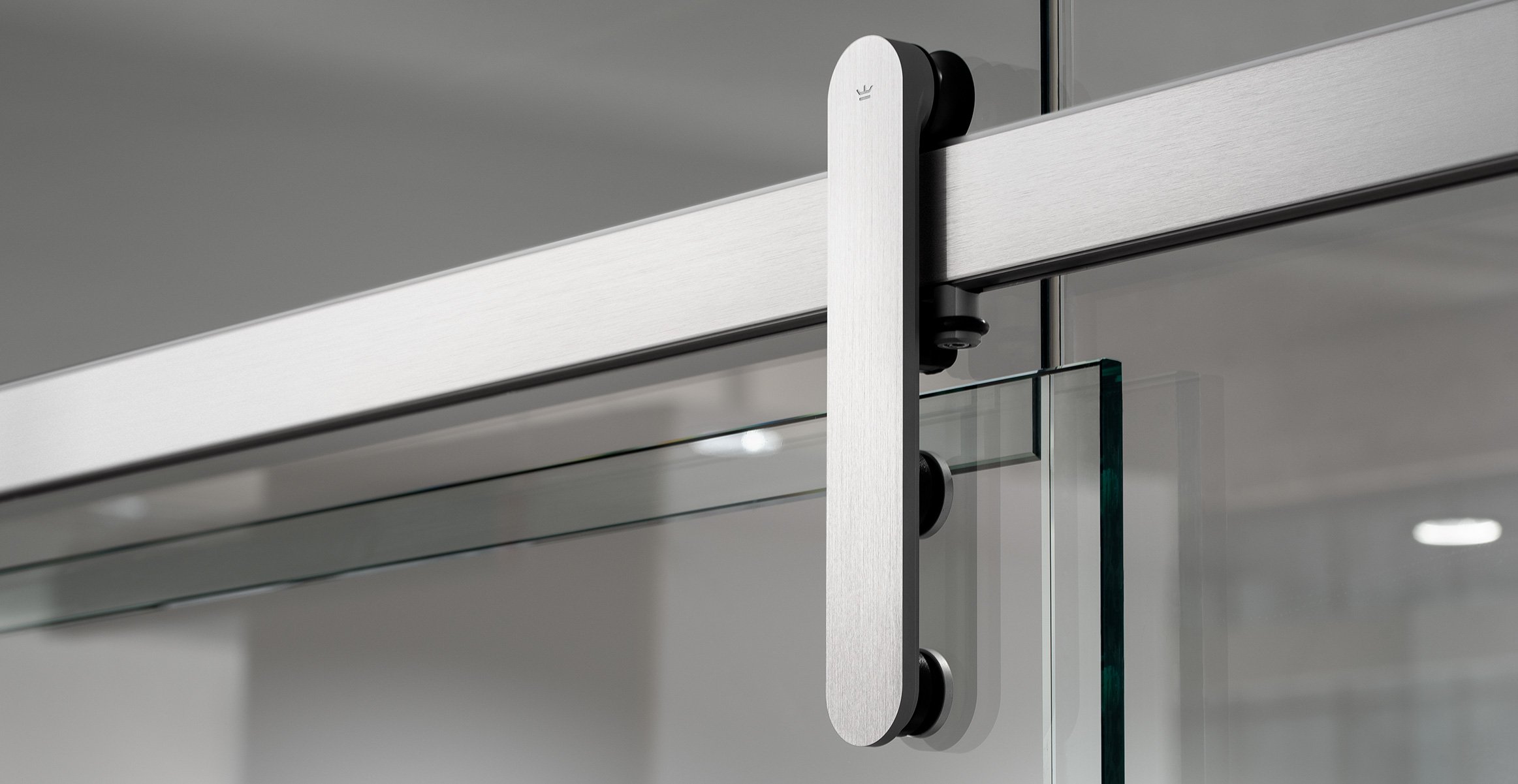 Close up modern sliding barn door hardware in brushed stainless finish mounted to glass door in office.