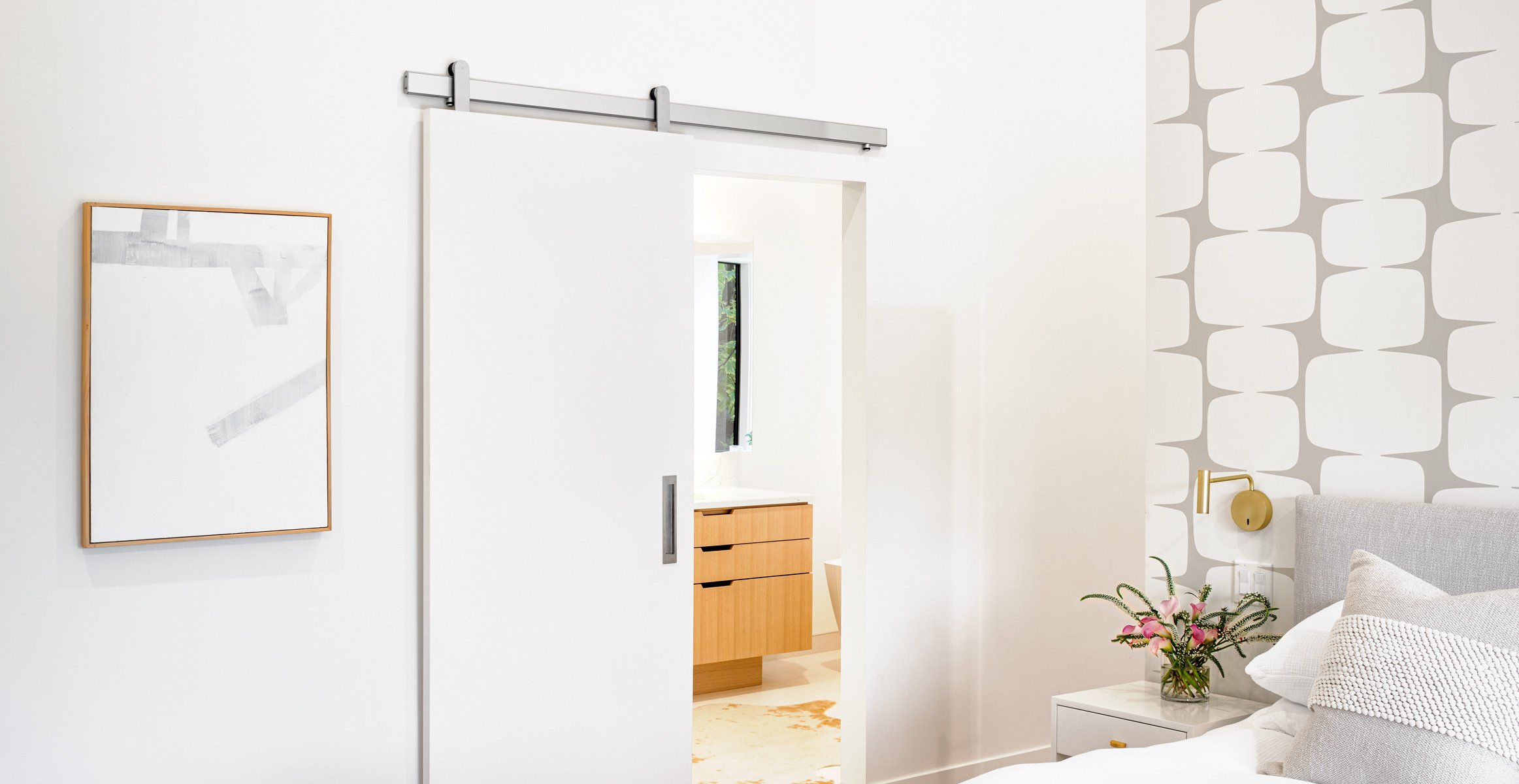 Modern sliding barn door hardware in brushed stainless finish from Krownlab with flat white door in elegant en suite bedroom.