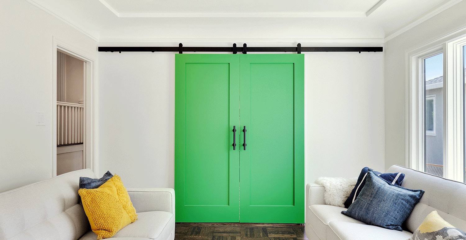 Modern sliding barn door hardware in black finish installed on green bi-parting kitchen doors in front of living room.
