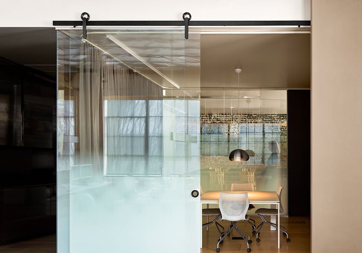 Baldur sliding barn door hardware installed in glass conference door in modern architecture office.